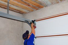 Contractor Installing Garage Door Post Rail and Spring Installation and Garage Ceiling.  Spring Tension Lifts  Metal Section Garage Door Panel that the Motor does not have to Lift Entire Weight.